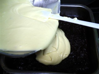 Pouring cheesecake batter onto brownie batter.