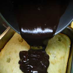 chocolate ganache being poured on yellow cak