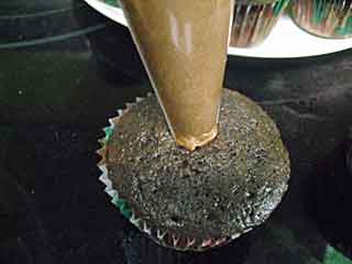Piping filling into chocolate cupcakes.