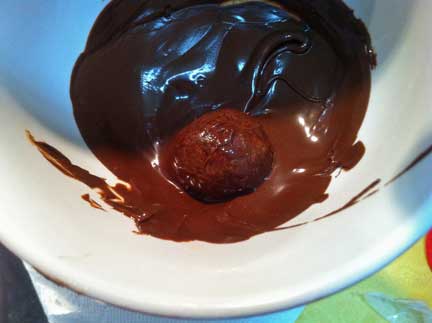 Peanut butter ball in a bowl being covered with chocolate.