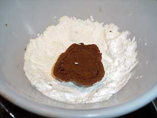 cooled meltaway cookie being dipped in powdered sugar